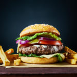 Craft beef burger and french fries on wooden table isolated on dark background.