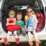 two little girls  and boy sitting in the car with backpacks