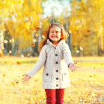 Happy little girl child having fun playing with yellow leafs in
