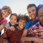 Six pre-teen friends piggybacking in a park, close up portrait