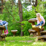 Two cute little sisters having fun on giant wooden mushrooms
