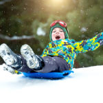 Boy sledding in a snowy forest. Outdoor winter fun for Christma