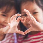 Two cute asian child girls making heart shape with hands togethe