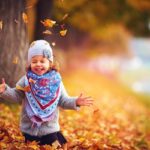 adorable happy girl playing with fallen leaves in autumn park