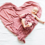 Smiling baby lying on a pink blanket in the shape of a heart