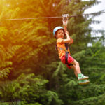 Happy kid with helmet and harness on zip line between trees