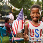 Young black boy holding flag at 4th July family garden party