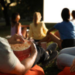 Young people with popcorn watching movie in open air cinema, closeup. Space for text