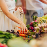 Female hands puts fruits and vegetables in cotton produce bag at food market. Reusable eco bag for shopping. Zero waste concept.