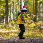 A little boy in a cap walks on a log