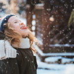 happy child girl catching snowflakes and playing on winter snowy walk in garden