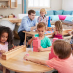 Teacher And Pupils Working At Tables In Montessori School