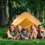 happy multicultural kids smiling while lying near camp