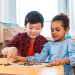 Children playing with wooden board game at table in montessori c