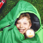 Preteen school kid boy in sleeping bag camping. Outdoors activity with children in summer. Fun and adventure camp, family and friends vacations or weekend trip. Portrait of child with flashlight.