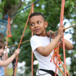 Little African-American boy climbing in adventure park. Summer c