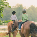 Kids learn to ride a horse near the river before sunset.