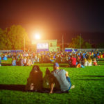 Summer cinema. People and couples watching a movie on the screen of a summer cinema in the evening