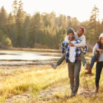 Parents Giving Children Piggyback Ride On Walk By Lake