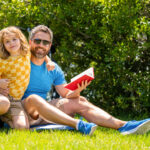 Father and son connect through stories in nature. Father and son bonding over literature. Father and son explore books in nature beauty. quality time for father and son. Outdoor learning, copy space