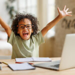 Little african american school boy raising hands up with excitement during home distance education