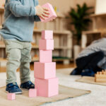 Cropped picture of a toddler building a tower with wooden blocks and playing games with montessori toys.