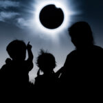 Silhouette back view of family looking at solar eclipse on dark sky