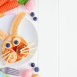 Easter Bunny breakfast pancakes on a white plate. Side border against a white wood background with copy space.