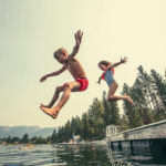 Kids jumping off the dock into a beautiful mountain lake. Having