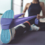 Resistance band exercise at home. Woman doing pilates workout using elastic strap pulling with arms for shoulder training on yoga mat indoors.