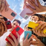 Young group of people using mobile phone device standing in circle outdoors