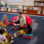 Friendly teacher reading a book to pupils during literature class