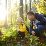 School boy and his father hiking together and exploring nature with magnifying glass. Child with his dad spend quality family time together in the sunny summer forest.
