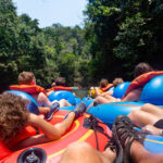Large group of people floating down a scenic jungle river in Belize Central America on a natural Cave Tubing adventure. Real people having real outdoor fun in the jungle. View from behind