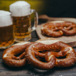 draft beer in the mugs and pretzels on dark wooden background