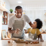 Cheerful smiling Black son enjoying playing with his father whil