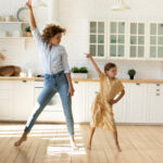 Mother and little daughter dancing to favorite music in kitchen