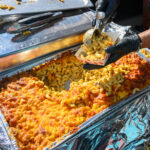 Hands Serving Jerk Chicken Mac and Cheese at the Poboy Festival on Oak Street in New Orleans, LA, USA