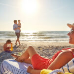 Chair, relax or kids with happy woman at beach on holiday vacation or weekend together with dad or family. Father, calm mother and children siblings at sea for bonding or break in nature in Spain