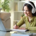 Happy teenage student e-learning and taking notes