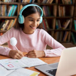 Happy indian school girl learning online class on video call on laptop.