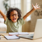Little african american school boy raising hands up with excitement during home distance education